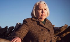 Susanna Clarke in winter coat with hand on stone wall.