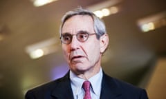 A thin, older white man in a suit and tie wearing glasses looks off to his right.