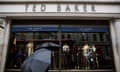 People shelter under umbrellas as they pass a Ted Baker shop