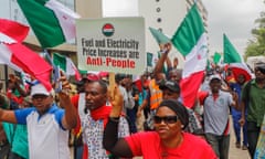 People march with Nigerian flags and a placard that reads ‘Fuel and Electricity Price Increases are Anti-People’