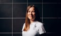 Head and shoulders shot of woman smiling against black tiled backdrop, wearing white polo shirt with Team GB logo
