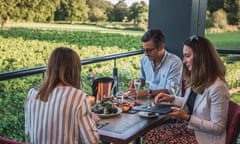 Visitors to the Ashling Park Estate vineyard in Sussex, UK, sit around a table on a veranda drinking wine and eating.