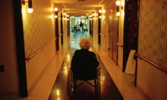 A woman in a wheelchair looking down a long dark corridor of an aged care home