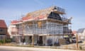 A half completed new home, surrounded by scaffolding and with no tiles yet on the roof, on a building site