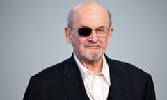 An older Indian man with gray hair and a gray goatee, in a black blazer and white shirt with no tie, wearing glasses with the right eye black.