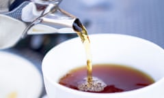 Someone pours hot black tea into a white cup from a restaurant-style kettle