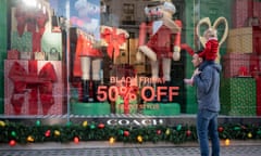 A man with a child on his shoulders looks at a Christmas window display