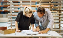 An apprentice carpenter discusses a blueprint with a colleague