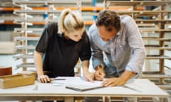 A male carpenter explaining a blueprint to a trainee in a workshop