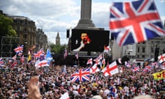 Trafalgar Square full of people waving UK and English flags as Tommy Robinson seen speaking on a screen