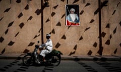 A man rides a motorcycle past a wall of the Nizwa fort bearing a portrait of the Omani Sultan before the first stage of the 2018 cycling Tour of Oman from Nizwa to the Sultan Qaboos University in Muscat on February 13, 2017. / AFP PHOTO / Philippe LOPEZPHILIPPE LOPEZ/AFP/Getty Images