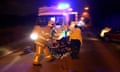 An injured person is wheeled to an ambulance by paramedics and firefighters after a road traffic accident