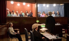 in a tv studio two adjacent juries behind glass look into a courtroom with two barristers and a seated woman