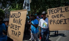 People hold signs that say 'world bank debt trap' and people over profit'.