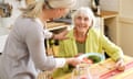 a woman hands a plate of food to a smiling 80 -year old woman at the dinner table