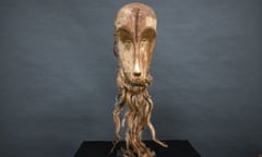 carved pale wooden mask with long, thin oval-shaped face and thick hair attached around the chin