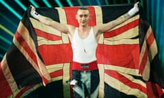 Olly Alexander in boxing costume holding a union flag over his head