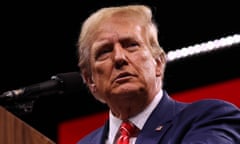 White man wearing blue suit and red tie stands at podium in front of microphone