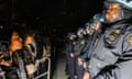 line of protesters in front of line of police wearing helmets in the dark