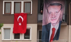 A woman sits on her balcony next to a banner featuring Turkish President Recep Tayyip Erdoğan