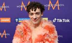 Nemo, wearing a peach and orange tulle top and eye gems, smiles at the camera at a press meeting