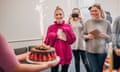 Two women are surprised with birthday cakes in the office.