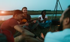 Group of young hikers camping in nature sitting in front of a fire