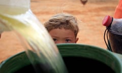 A young Brazilian boy watches as his mother collects water in a barrel.