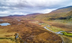 Mountains rise above a river surrounded by brown and green grassland