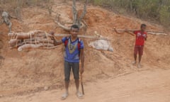 Two boys carrying bundled yams on their shoulders on a road in Madagascar.