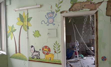 A cracked wall with cartoon trees and a zebra, lion and monkey on it. Through an open doorway is a room covered in rubble, with water gushing down from the ceiling.