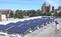 Solar panels on a roof with buildings and trees in the background.