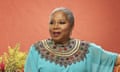 An older African woman with cropped grey hair wearing a turquoise blouse with an intricately embroidered collar