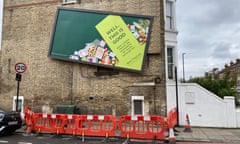 The wonky billboard on the side wall of a brick house with safety fencing blocking off the pavement below