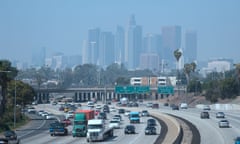 Dense traffic on a highway, with skyscrapers in smog in the background