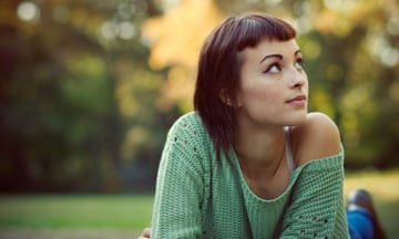Young woman looking up with autumn background<br>Young woman with short bangs and green sweater looking up with bright autumn background.