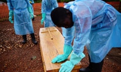 Sierra Leonese government burial team members wearing protective clothing stand next to a coffin