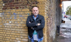 A burly man leaning against a brick wall.