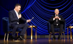 two men in suits sit on stage