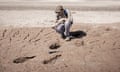 Geologist Maximiliano Rueda crouches on a dried mud beach next to dinosaur footprints