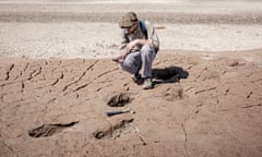 Geologist Maximiliano Rueda crouches on a dried mud beach next to dinosaur footprints