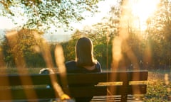 Woman sitting alone on a bench in a park during sunset