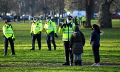 A police officer wearing a mask speaks to two young children in a park.