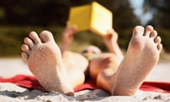 Woman lying on beach reading book (focus on bottom of sandy feet)