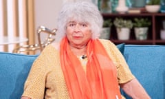 Miriam Margolyes sits on a blue sofa wearing a yellow top and an orange scarf
