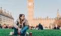 Pensive woman listening to earbuds seated on grass near parliament