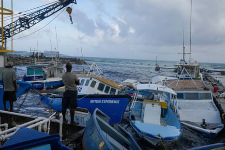 Tall barefoot Black men in T-shirts and shorts look out over a harbor, with a dozen boats crammed together in the water.