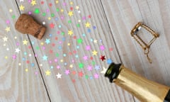 Overhead of a bottle of champagne with the cork popping on a rustic wood table. The spray from the bottle is stars of various si<br>ECWY1X Overhead of a bottle of champagne with the cork popping on a rustic wood table. The spray from the bottle is stars of various si