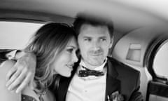A black and white photo of a woman and a man sitting in the backseat of a car on their wedding day - they look glamorous and happy.