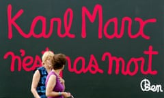 Women walk past a giant billboard that reads " Karl Marx is not dead"  north of Paris